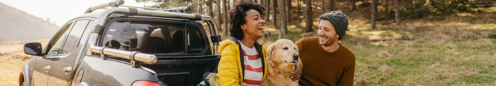 Couple smiling while sitting with their dog in the back of their truck.