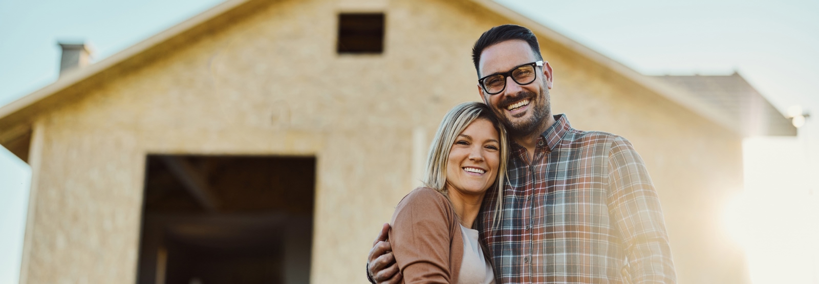 young couple poses for picture in front of a house still under construction