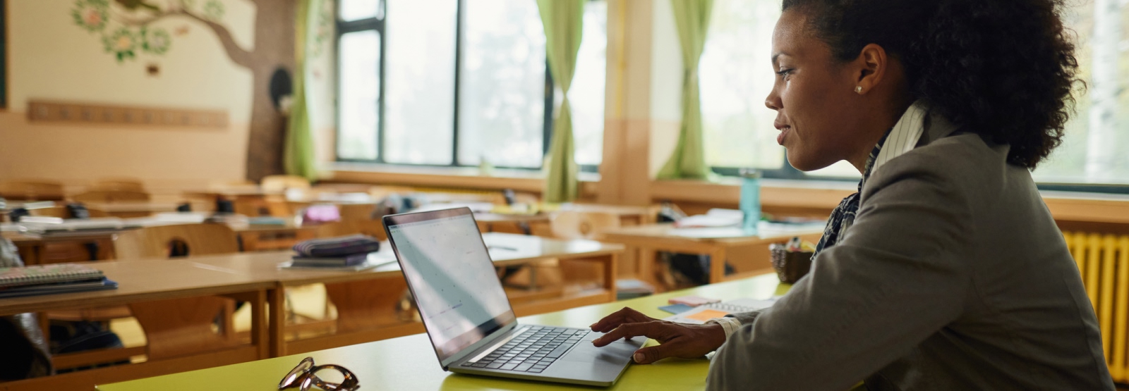 teacher in an empty classroom using a laptop